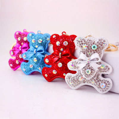 Four jeweled teddy bear keychains in pink, blue, red, and white are arranged together.