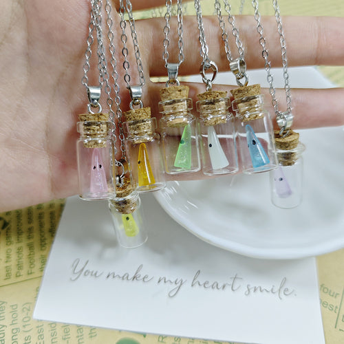 Hand holding six mini ghost bottle necklaces in mixed pastel colors