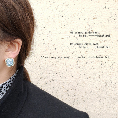 Teal shell square stud worn on ear against textured wall