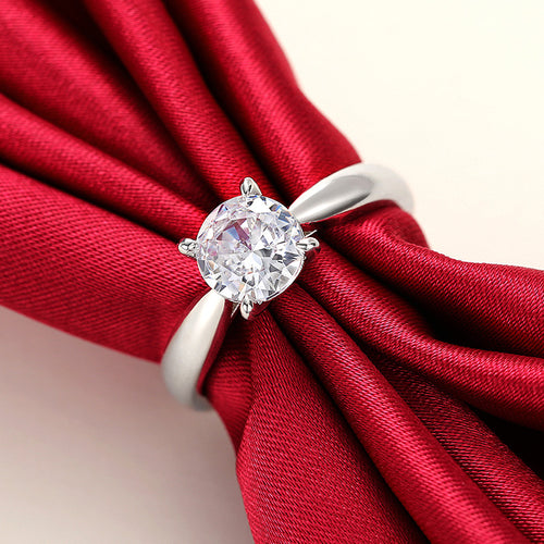Silver four prong clear stone ring displayed on red fabric knot