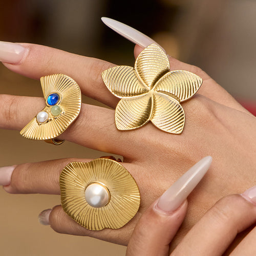 Three gold statement rings worn: fan with stones, flower, pearl disc