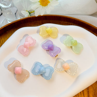 Seven glitter resin bow hair clips in pastel colors on white tray