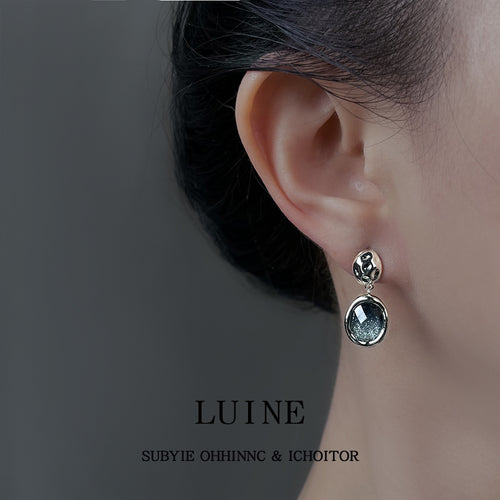 Silver-tone openwork-top blue-gray-round-stone studs shown worn on an ear.