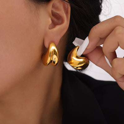 Model wearing gold geometric teardrop stud holding matching earring