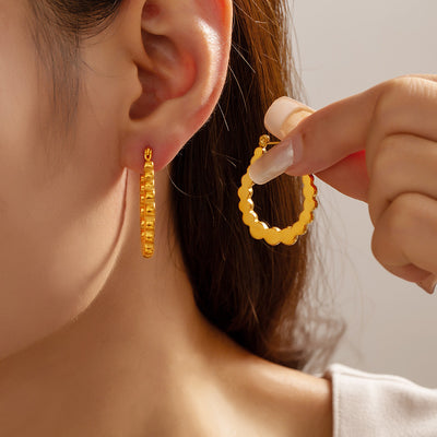Model holding a gold scalloped U-hoop earring next to matching ear
