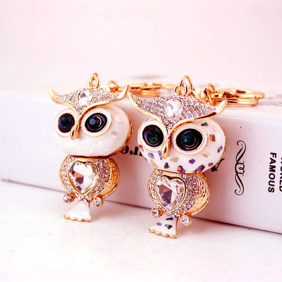 Two gold-tone owl keychains display white and multicolor face details side by side.