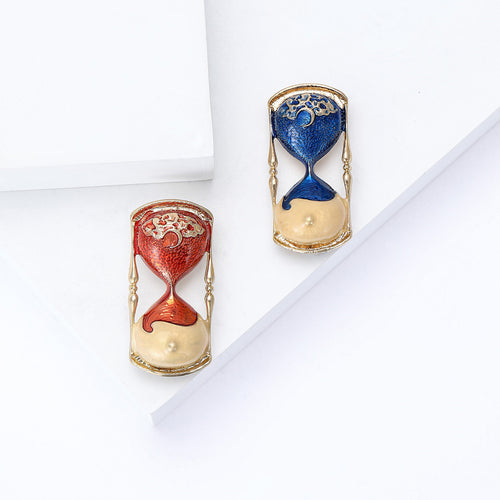 Red and blue enamel hourglass brooches displayed together on white blocks
