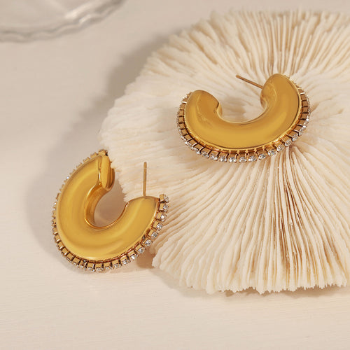 Pair of gold C-shape crystal-rim earrings on white coral display