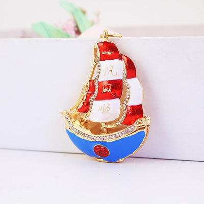 Close view of a sailboat charm with striped red and white sails and a blue hull.