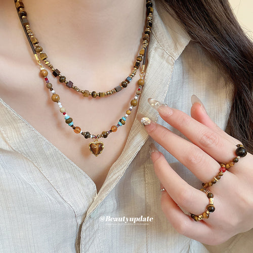 Model wearing layered brown beaded necklaces with heart pendant and brown bead rings