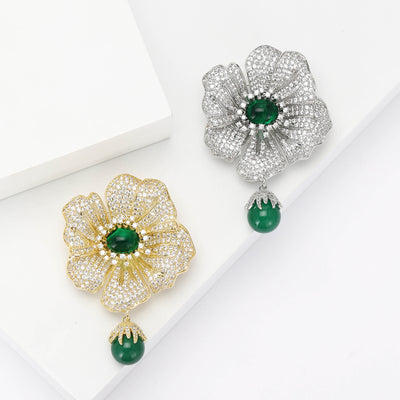 Front view of the green center flower brooch with hanging bead with polished metal detail on a white background