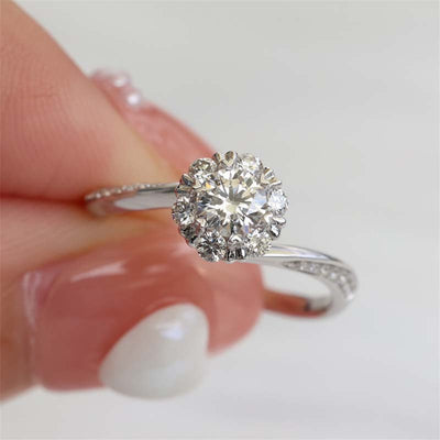 White gold round halo clear stone twist band ring held between fingers