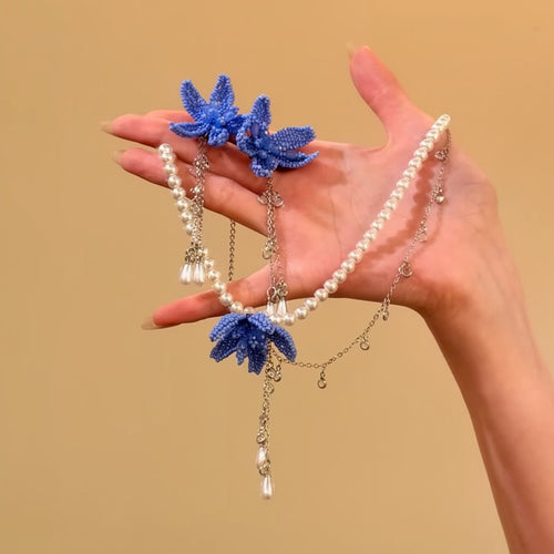 Blue seed-bead flower earrings and pearl necklace held in open hand