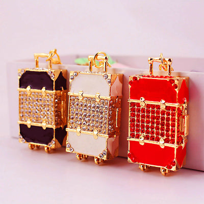 Three suitcase-shaped charms in black, white, and red stand side by side.