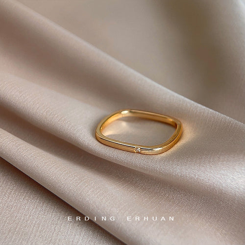 Gold rounded square ring lying on soft pink fabric