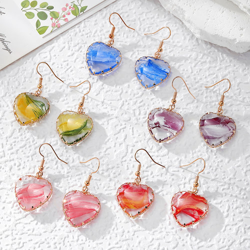 Five pairs of wire-wrapped heart gradient resin earrings on white textured surface