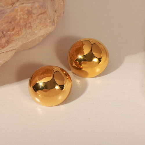 Pair of gold dome earrings on light surface with stone