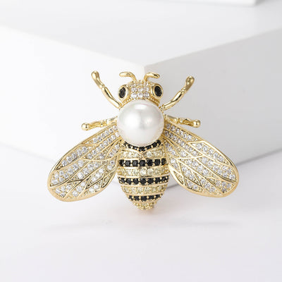 Front view of gold tone bee brooch with pearl body and crystal-lined wings against a white background.