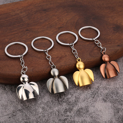 Four angel figure keychains in polished silver, antique silver, gold, and copper finishes on wood.