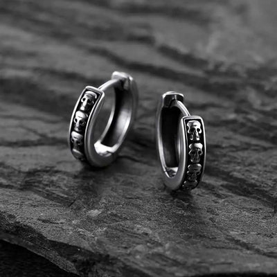 Pair of silver skull carved huggie hoop earrings on dark stone