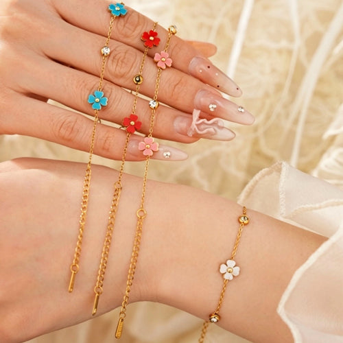 Four gold flower bracelets held between fingers and white flower on wrist