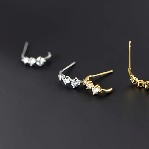 Silver and gold curved three-stone studs on dark surface with post backs