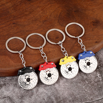 Four brake disc caliper keychains with black, red, yellow, and blue details on a wooden surface.