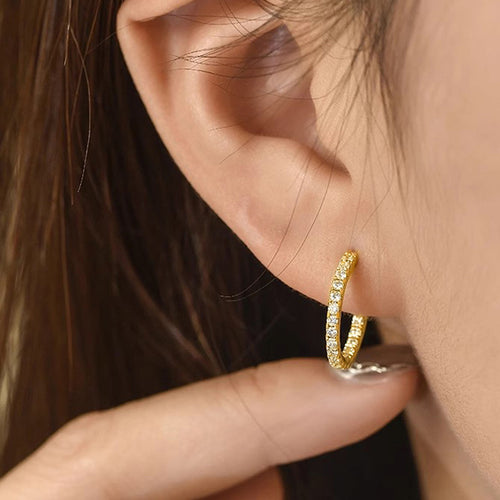 Angled detail view of gold tone open hoop earrings with rows of clear stones