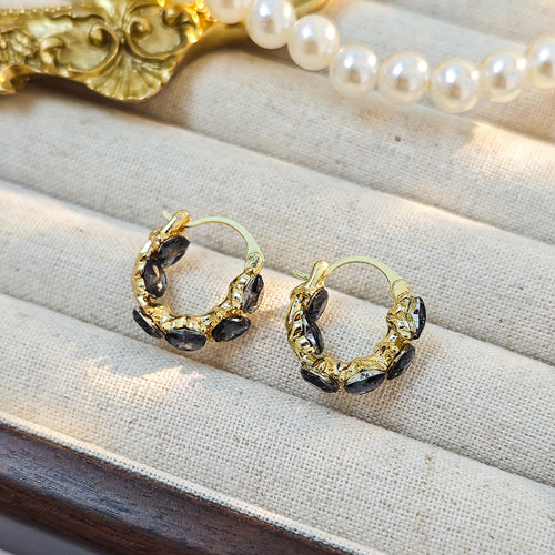 Gold mini hoop earrings with black heart crystals on beige jewelry tray