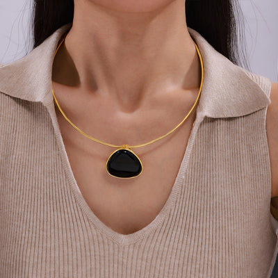 Gold snake chain black triangle pendant worn on collarbone over beige top