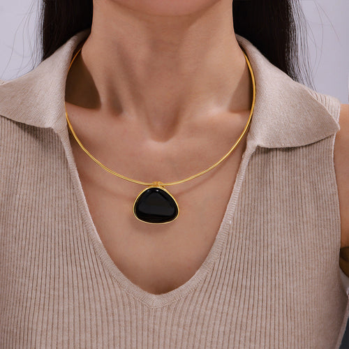 Gold snake chain black triangle pendant worn on collarbone over beige top