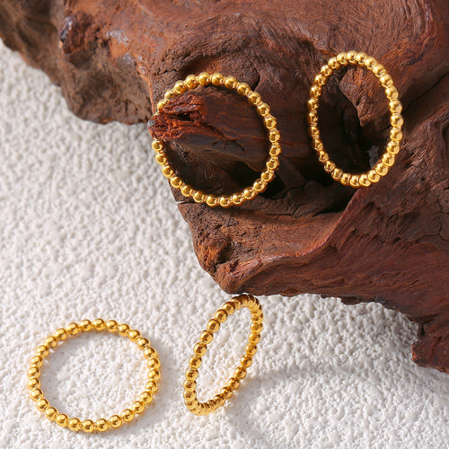 Four gold beaded ball rings displayed on wood and white textured surface