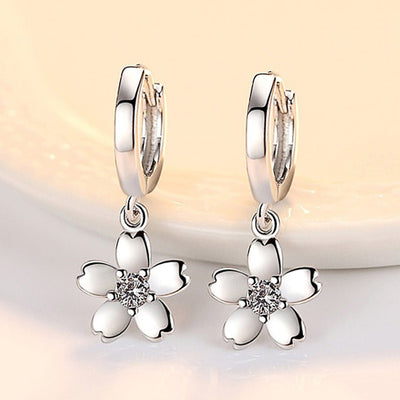 Front view of white flower charm huggie hoop earrings in silver tone
