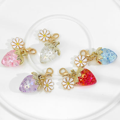 Five translucent resin strawberry charms with daisy accents laid out together