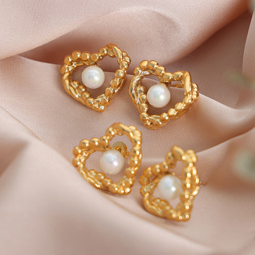 Four gold heart open frame pearl stud earrings on pink satin fabric