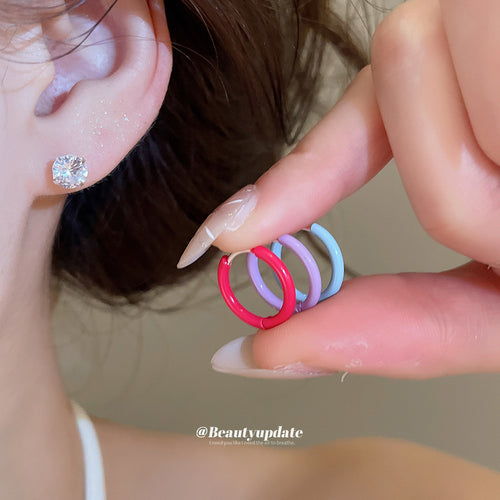 Three enamel huggie hoops held near ear with clear crystal stud worn