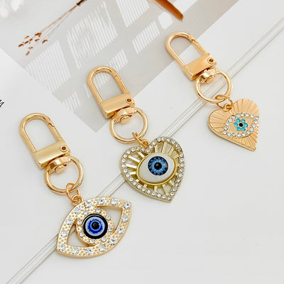 Three gold-tone evil eye keychain designs shown together on a marble surface