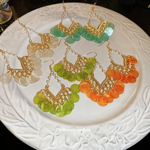 Gold tone openwork chandeliers with translucent white shell sequins displayed on a jewelry surface