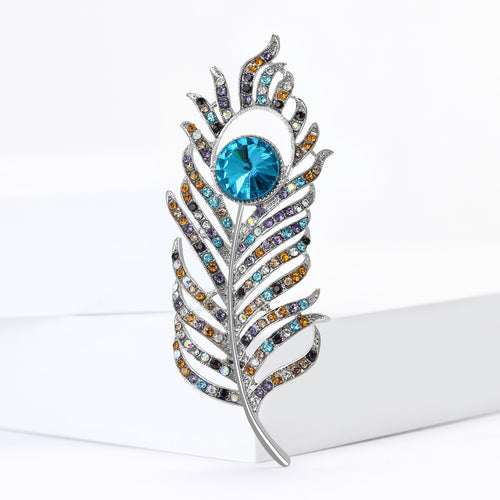 Peacock feather brooch upright on white geometric blocks