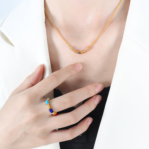 Gold curved bar necklace blue stone worn with white blazer