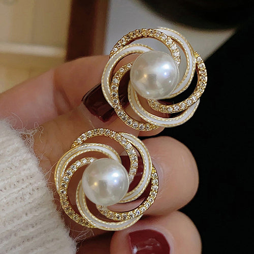 Pair of gold white pearl crystal swirl studs close-up in hand
