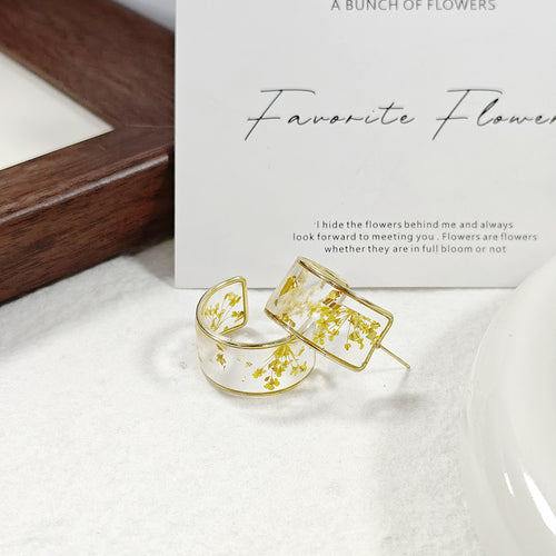 Yellow dried flower clear resin hoop studs with gold foil beside frame