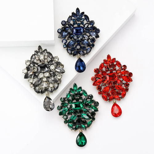 Angled display of the oval floral crystal dangle brooch on a white surface