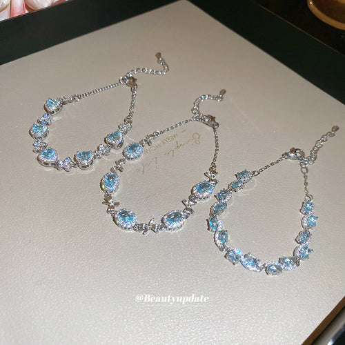 three pale blue crystal bracelets with oval, heart, or mixed center stones shown worn in a styled second view