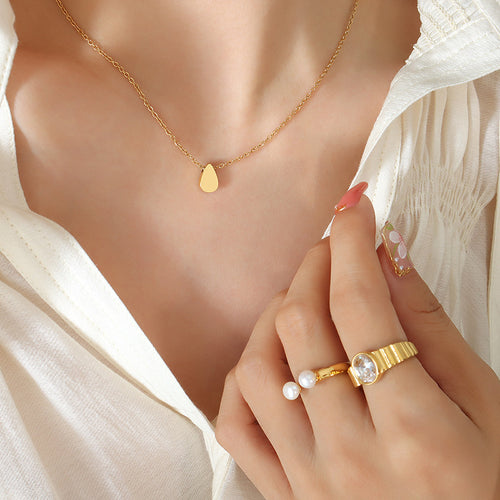 Gold teardrop pendant necklace worn on model with rings