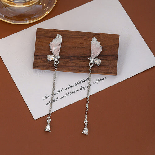 Pink butterfly chain drop earrings on wood block over card