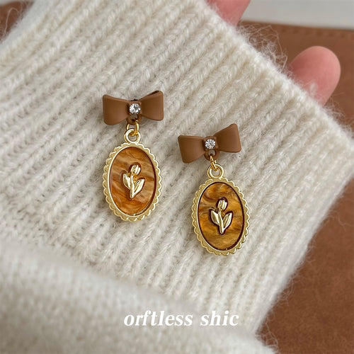 Brown bow oval tulip drop earrings on cream knit