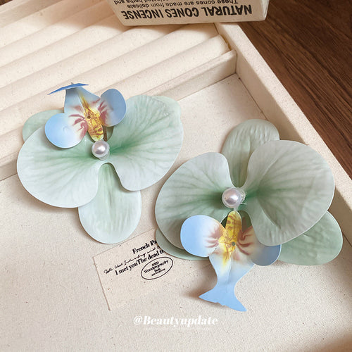 pale green and blue orchid hair clip with a pearl-like center shown worn in a styled second view