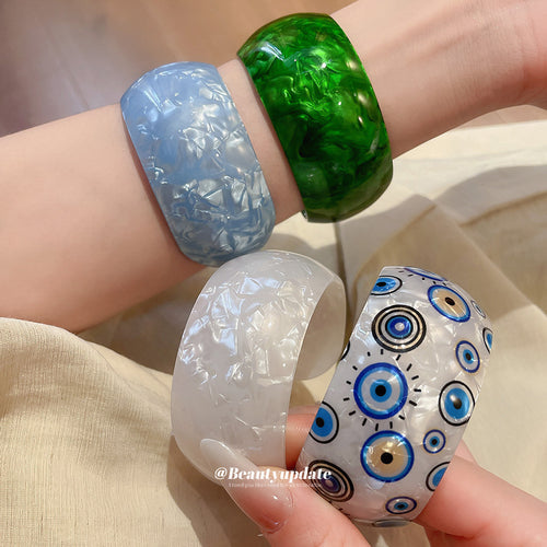 Wrist stack of blue green white marble and eye-print acrylic open cuffs
