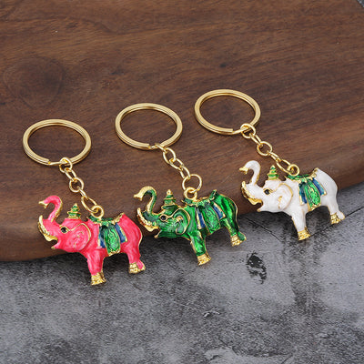 Three pink, green, and white elephant keychains displayed on a wooden surface.